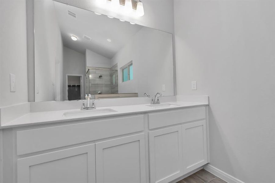 The primary bathroom offers a dual-sink vanity with ample counter space and sleek, modern fixtures. The large mirror and overhead lighting ensure that this space is as functional as it is stylish, perfect for starting your day with ease. The elegant design and high-quality finishes make this bathroom a true highlight of the home. **This image is from another Saratoga Home - Wren floorplan.**