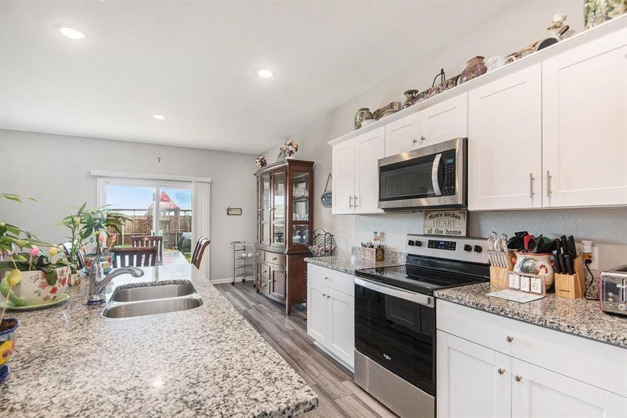 Kitchen featuring light stone countertops, appliances with stainless steel finishes, sink, light wood-type flooring, and white cabinets