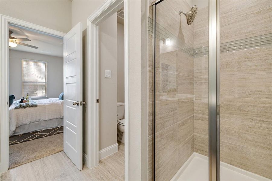 Bathroom featuring ceiling fan, hardwood / wood-style flooring, a shower with shower door, and toilet