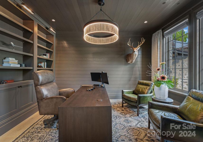 The study has custom built-in cabinetry and shelving with shiplap covered walls and ceilings with a one-of-a-kind chandelier as the focal point and library lighting for the perfect touch.