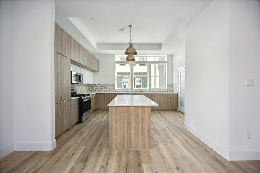 This modern kitchen features sleek cabinetry, stainless steel appliances, a central island, and upgraded flooring, complemented by ample natural light from large windows.