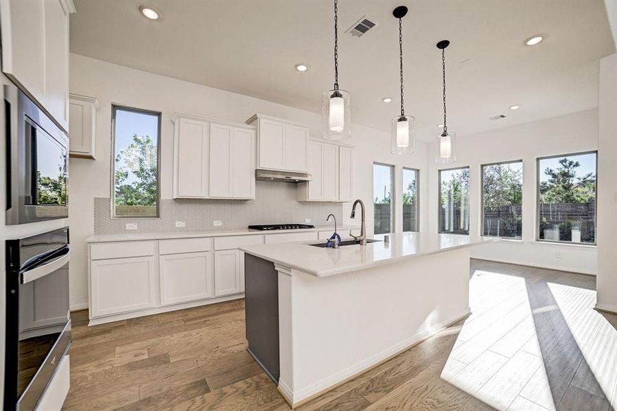 Large kitchen island with built in sink, space for barstools on opposite side, glass pendant lighting and light cabinets.