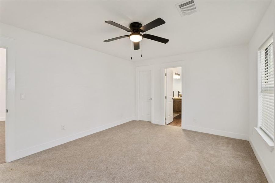 Unfurnished bedroom featuring light carpet, ensuite bath, and ceiling fan