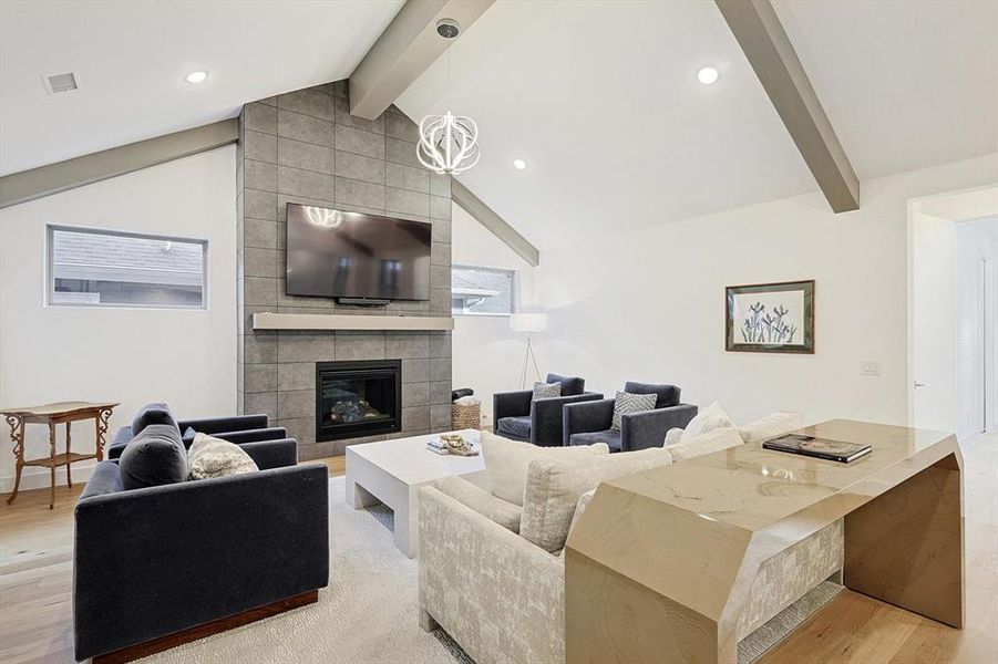 Living room featuring light hardwood / wood-style flooring, vaulted ceiling with beams, a fireplace, and an inviting chandelier