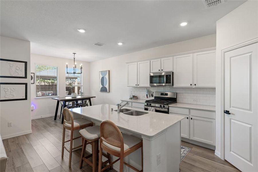 Kitchen with a center island with sink, an inviting chandelier, stainless steel appliances, and white cabinets