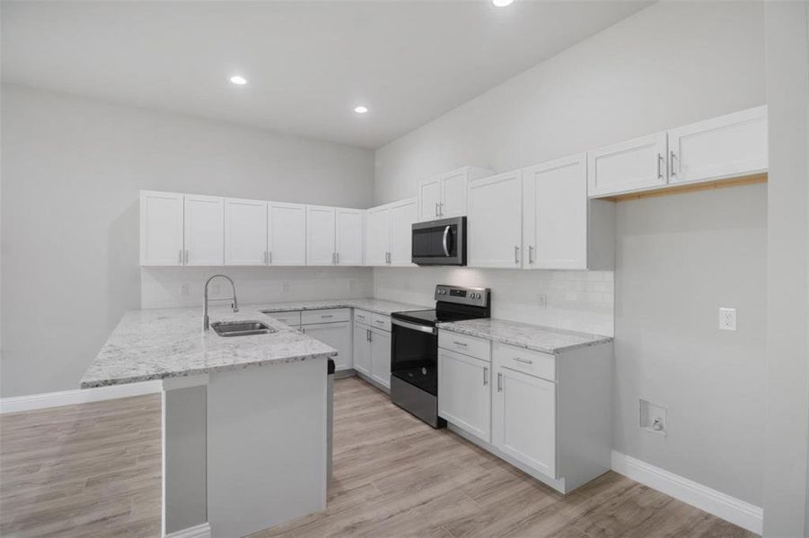 Kitchen with white cabinetry, light wood-type flooring, sink, appliances with stainless steel finishes, and kitchen peninsula