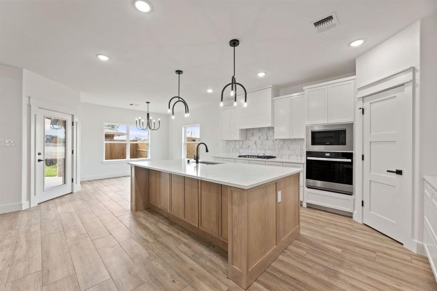 Kitchen featuring tile flooring, a center island with sink, tasteful backsplash, microwave, and stainless steel oven