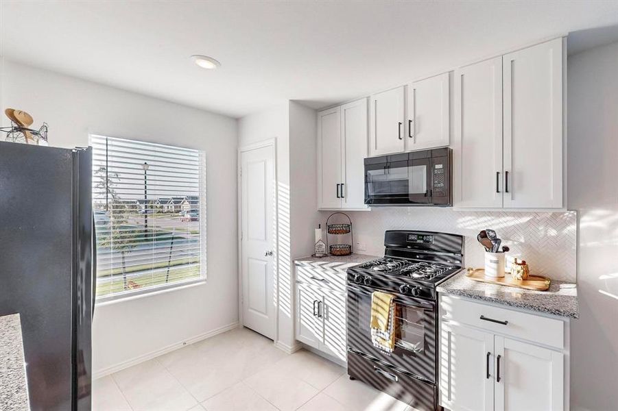 Kitchen with light stone counters, white cabinets, light tile patterned flooring, and black appliances