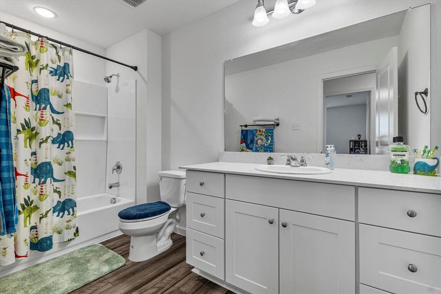 Full bathroom featuring vanity, shower / bathtub combination with curtain, hardwood / wood-style flooring, and toilet