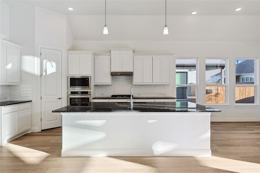 Kitchen featuring an island with sink, decorative backsplash, and light hardwood / wood-style floors