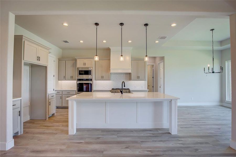 Kitchen with hanging light fixtures, tasteful backsplash, light wood-type flooring, appliances with stainless steel finishes, and sink