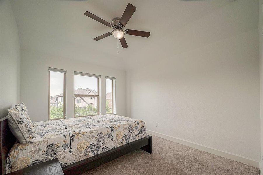 This is a bright, airy bedroom with a vaulted ceiling, equipped with a ceiling fan, and features a row of windows offering plenty of natural light and views of the neighborhood.
