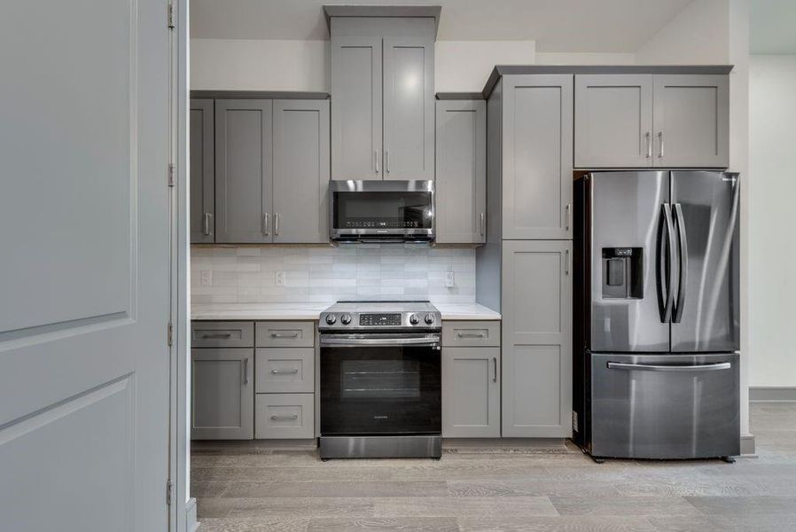 Kitchen featuring gray cabinetry, stainless steel appliances, light hardwood / wood-style floors, and tasteful backsplash