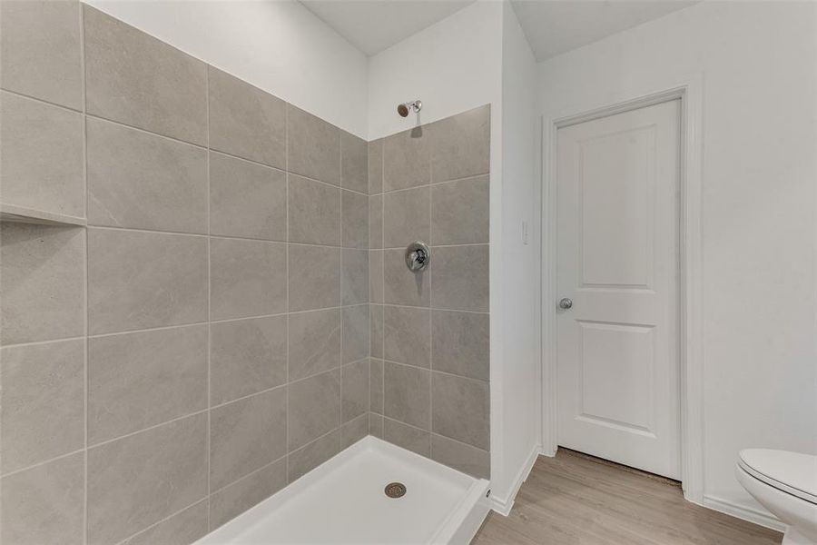 Bathroom with wood-type flooring, toilet, and tiled shower