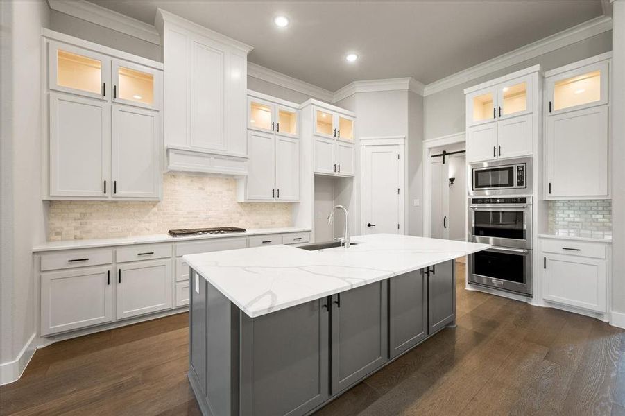 Kitchen featuring qts counters, center island with sink, wood flooring, and transom custom cabinets!