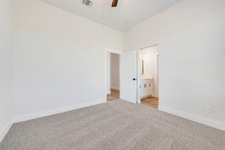 Unfurnished bedroom with connected bathroom, ceiling fan, and light colored carpet