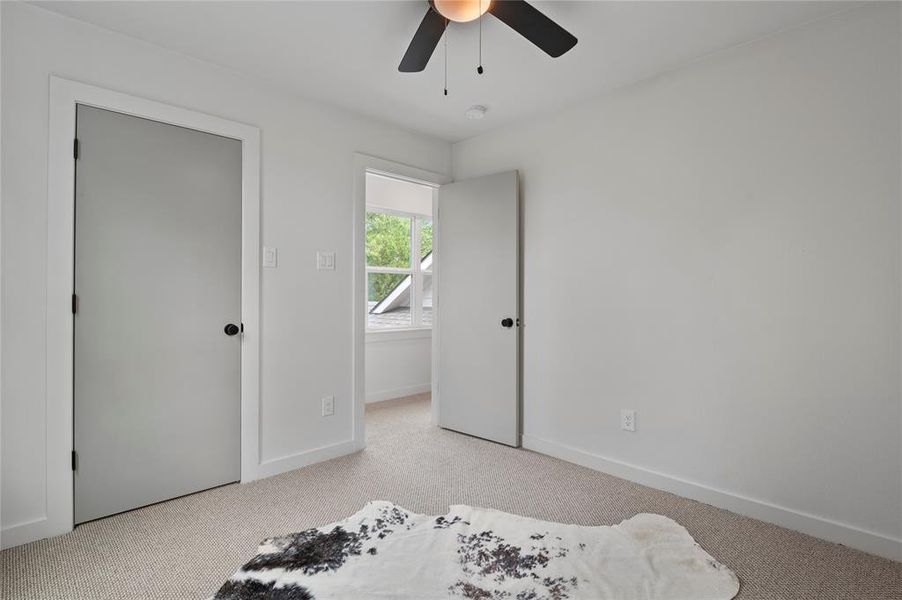 Bedroom with light colored carpet, ceiling fan, oversized closet.