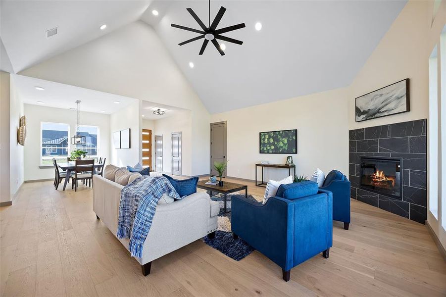 Living room with light hardwood / wood-style flooring, high vaulted ceiling, a tile fireplace, and ceiling fan with notable chandelier