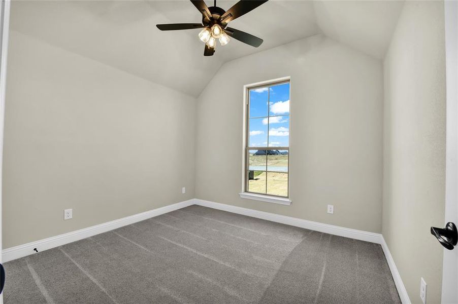 Spare room with ceiling fan, carpet flooring, and vaulted ceiling