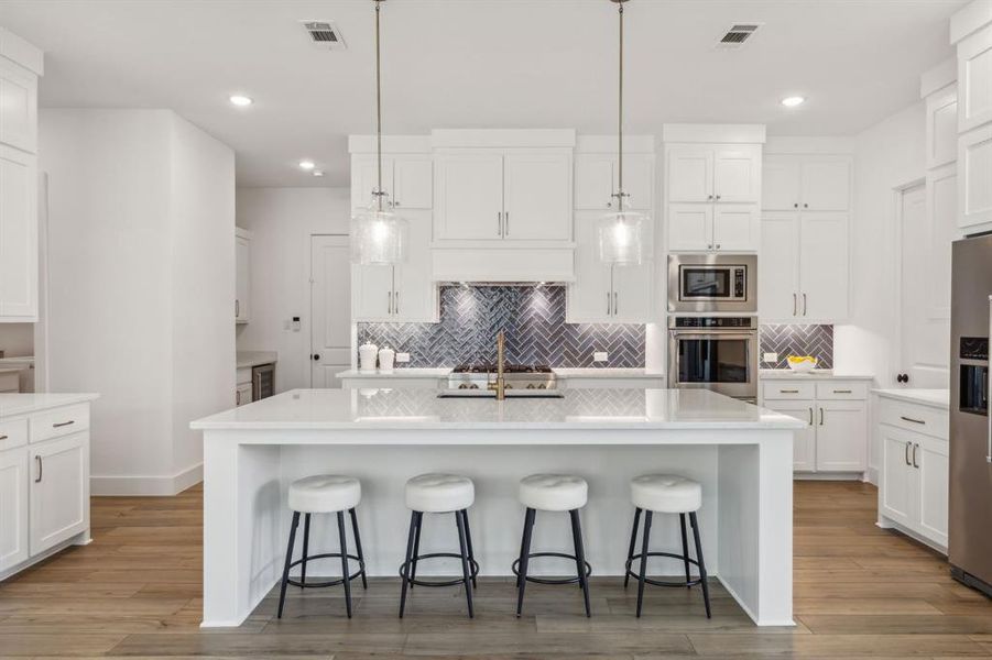 Kitchen with white cabinets, stainless steel appliances, light hardwood / wood-style floors, and an island with sink