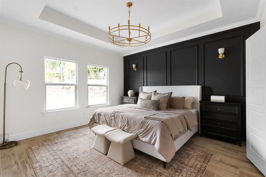 Bedroom with a tray ceiling, light wood-type flooring, ornamental molding, and a notable chandelier