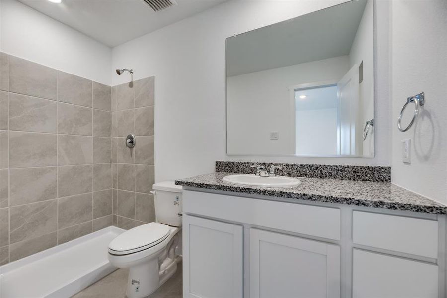 Bathroom featuring toilet, vanity, and a tile shower