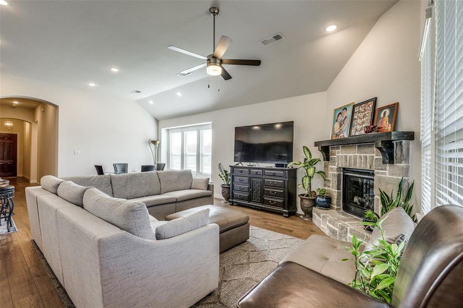 Living room with a stone fireplace, vaulted ceiling, ceiling fan, and light hardwood / wood-style flooring