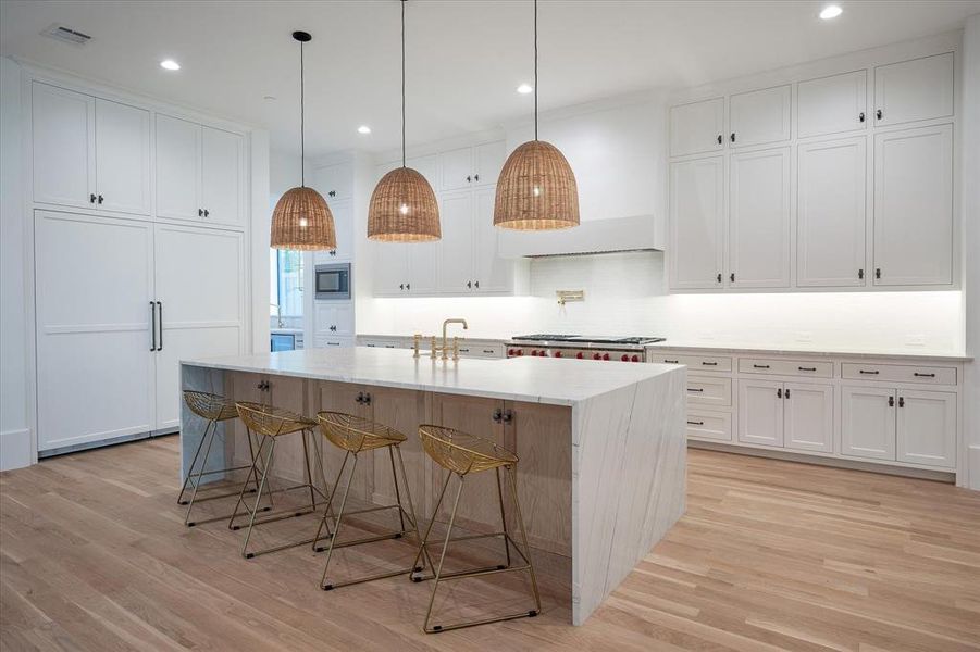 Kitchen featuring a kitchen island with sink, light wood-type flooring, decorative light fixtures, and white cabinets