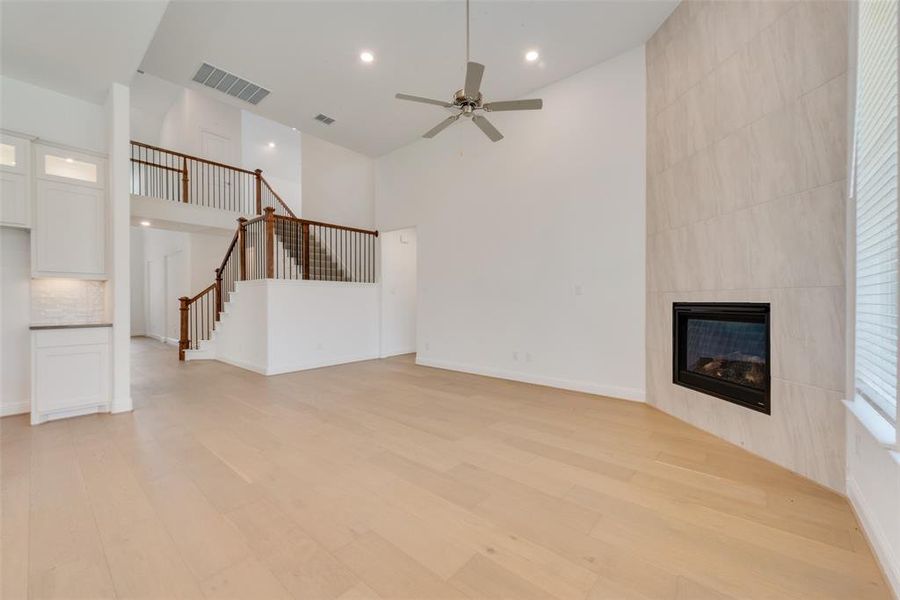 Unfurnished living room with high vaulted ceiling, a tiled fireplace, ceiling fan, and light wood-type flooring