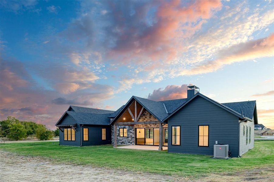 Back house at dusk featuring central AC, a yard, and a patio area