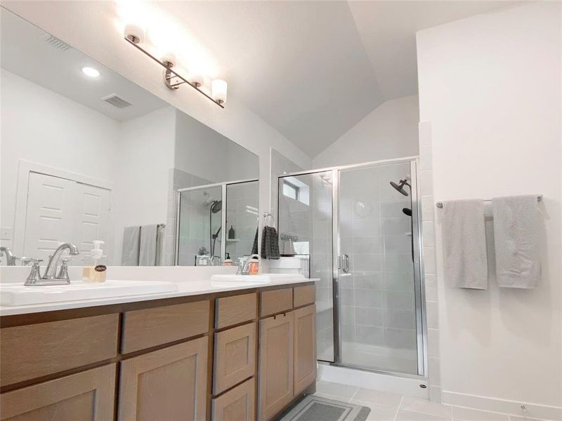 Bathroom featuring dual vanity, a shower with door, tile patterned flooring, and vaulted ceiling
