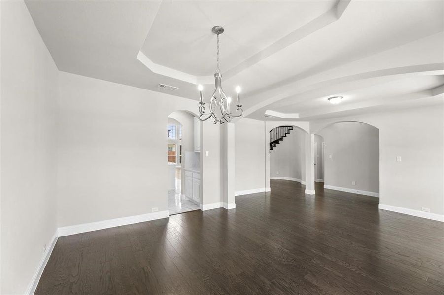 Empty room with an inviting chandelier, a raised ceiling, and dark hardwood / wood-style flooring