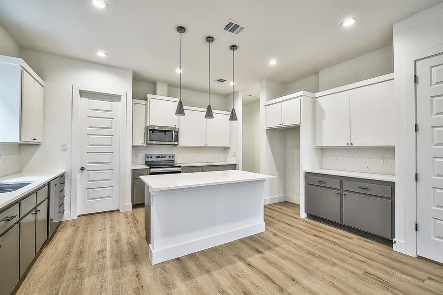 Kitchen with white cabinets, a kitchen island, stainless steel appliances, and light hardwood / wood-style floors