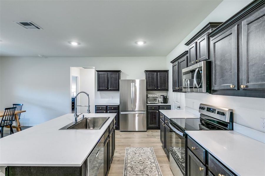 Kitchen featuring light hardwood / wood-style floors, stainless steel appliances, a center island with sink, and sink