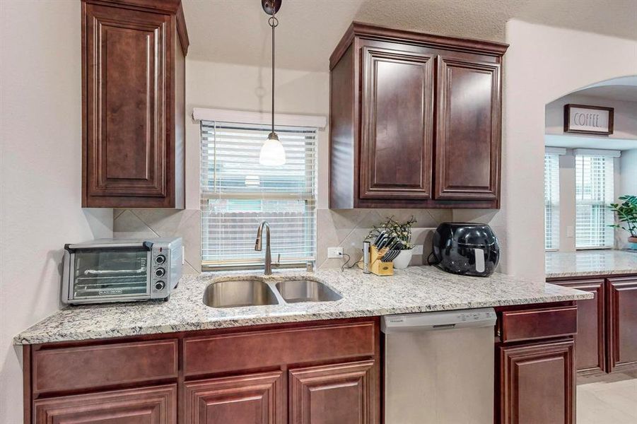 Kitchen featuring dishwasher, decorative backsplash, sink, light stone countertops, and pendant lighting