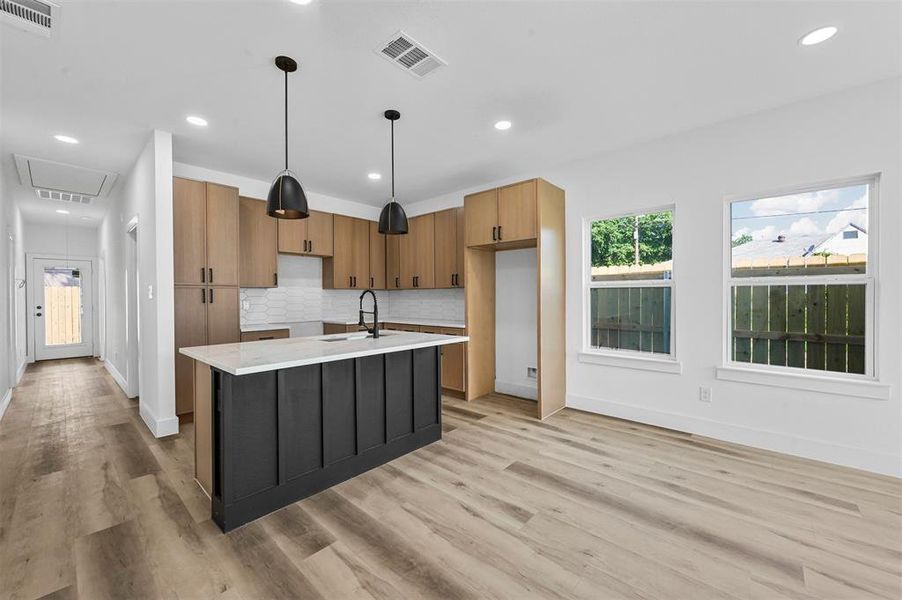Kitchen featuring tasteful backsplash, a kitchen island with sink, light wood-type flooring, sink, and pendant lighting