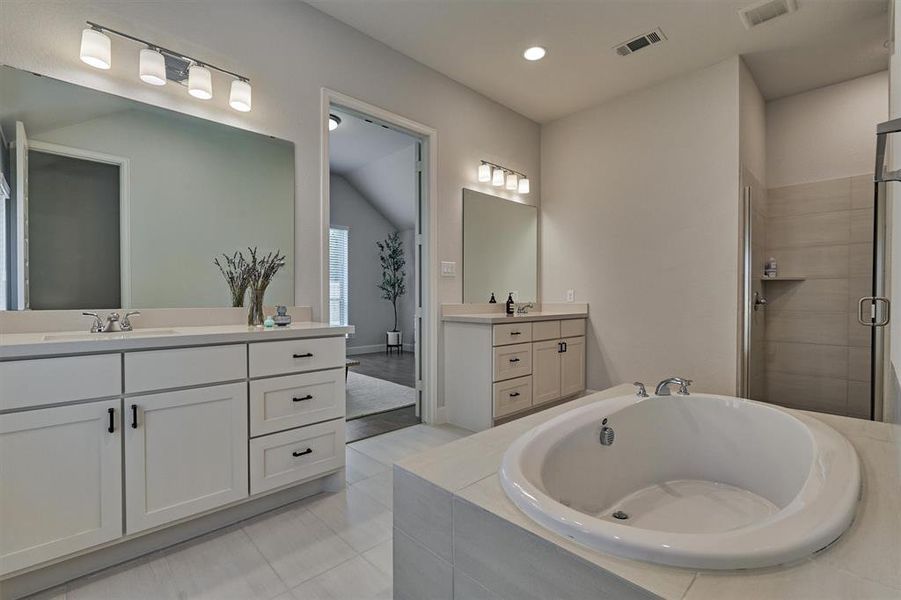 Luxurious primary bath offers oversized soaking tub, dual vanities with ample storage, and separate stall shower with complementary tile surround.