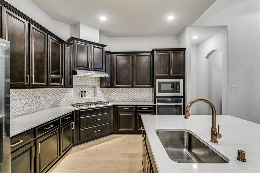 Kitchen with sink, stainless steel appliances, dark brown cabinetry, decorative backsplash, and light hardwood / wood-style flooring