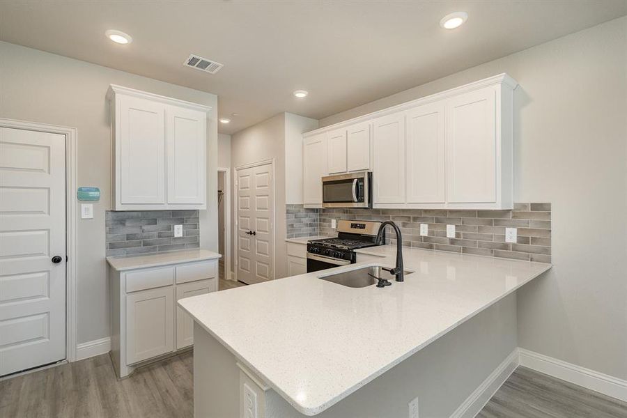 Kitchen with light hardwood / wood-style flooring, kitchen peninsula, stainless steel appliances, white cabinetry, and tasteful backsplash