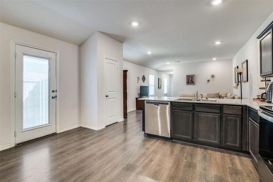 Kitchen with appliances with stainless steel finishes, dark brown cabinets, hardwood / wood-style floors, and sink