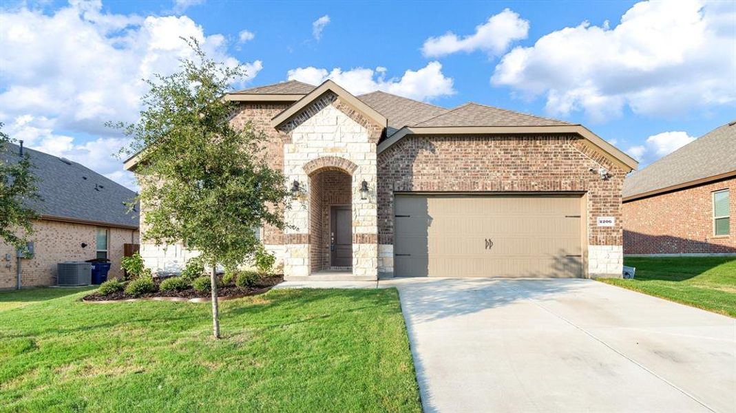 View of front of house with cooling unit, a garage, and a front lawn