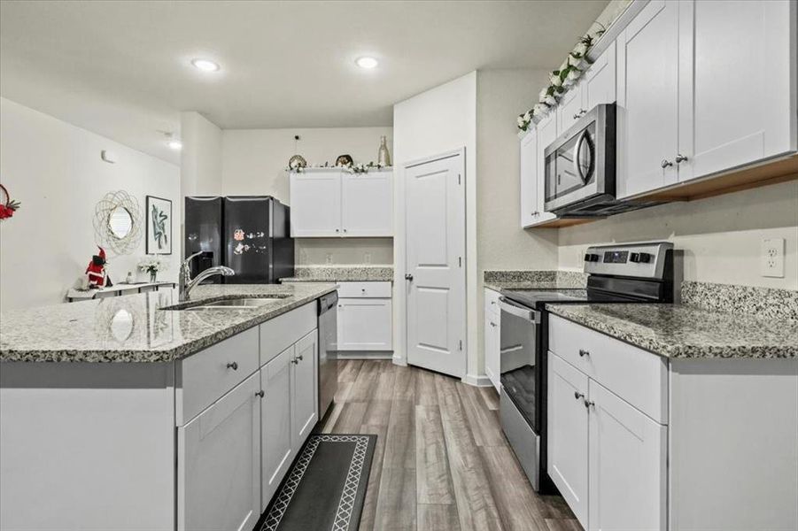 Kitchen featuring white cabinetry, sink, stainless steel appliances, a kitchen island with sink, and hardwood / wood-style flooring