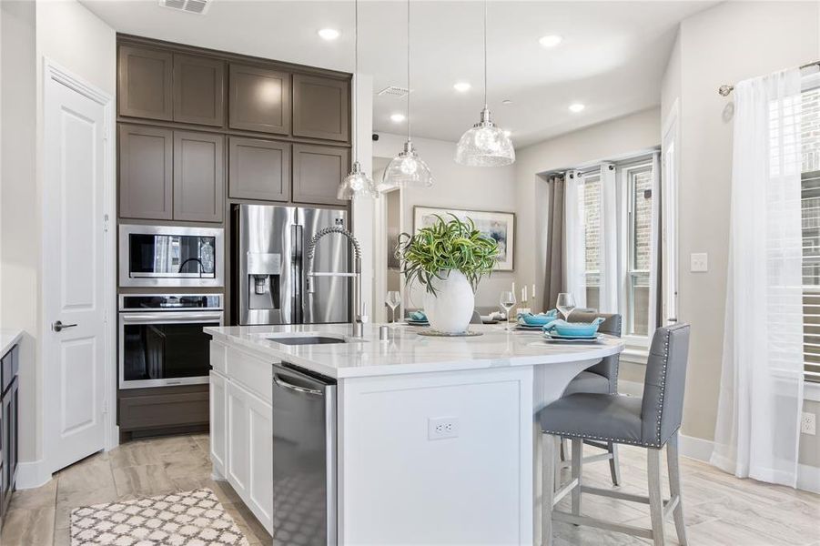 Kitchen featuring an island with sink, stainless steel appliances, pendant lighting, light stone counters, and white cabinetry