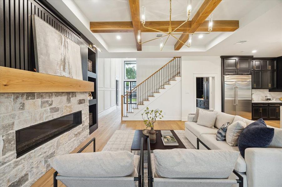 The family room features decorative wood beams, a brass chandelier and a linear fireplace with stone and reeded wood surround.