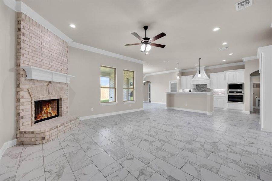 Unfurnished living room featuring a fireplace, ceiling fan, and crown molding