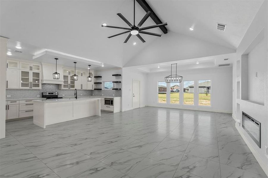 Unfurnished living room with ceiling fan with notable chandelier, beam ceiling, sink, and high vaulted ceiling