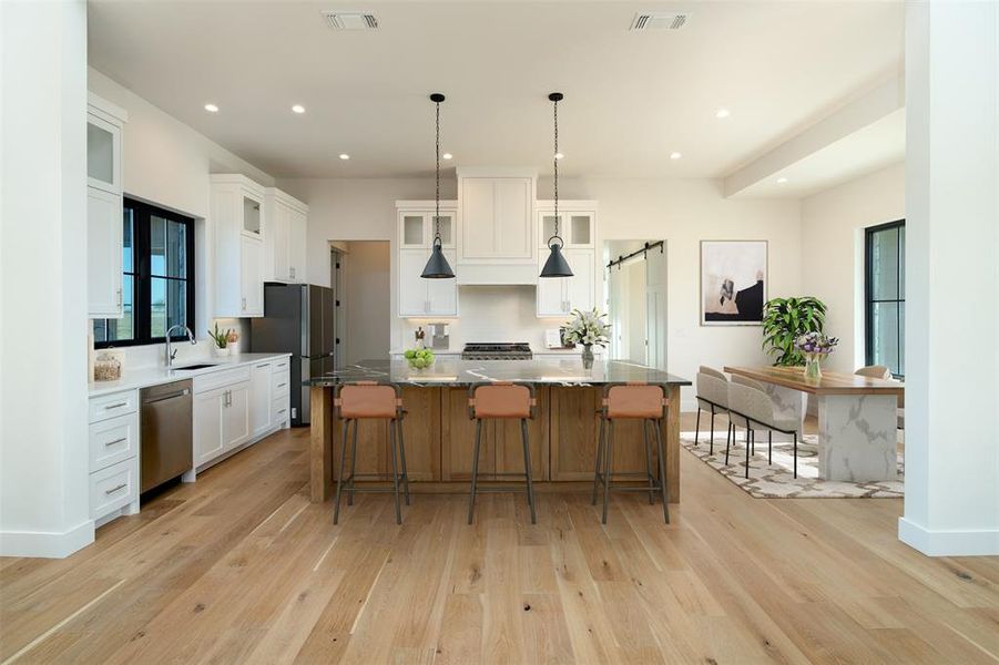 Virtually staged kitchen with appliances with stainless steel finishes, a spacious island, hanging light fixtures, white cabinetry, and light stone counters