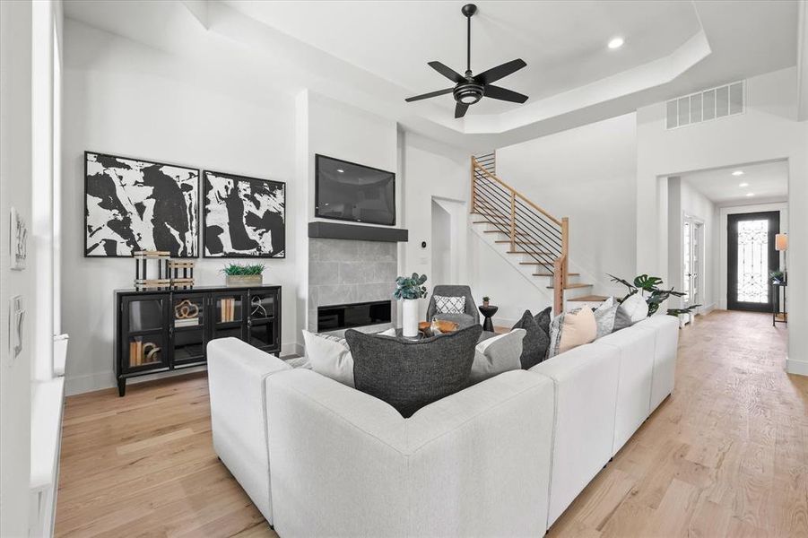 Living room with light hardwood / wood-style flooring, ceiling fan, a tiled fireplace, and a raised ceiling