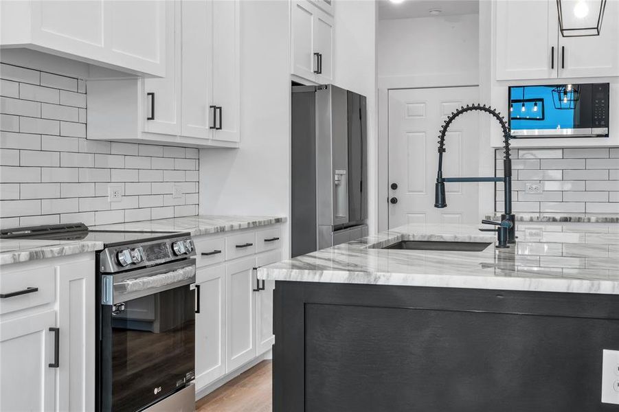 Kitchen with light stone countertops, sink, white cabinetry, stainless steel appliances, and backsplash