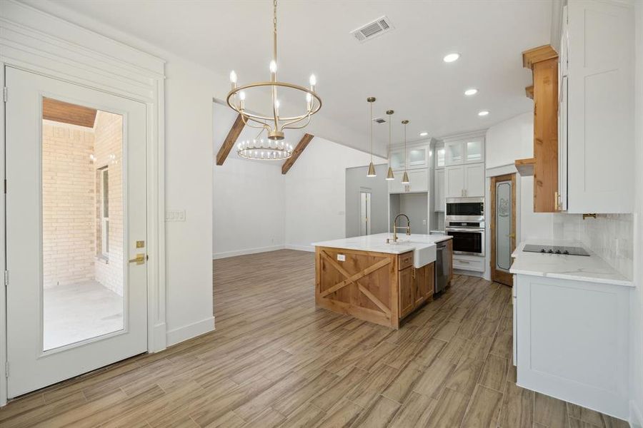 Kitchen with a kitchen island with sink, hanging light fixtures, sink, light wood-type flooring, and white cabinetry